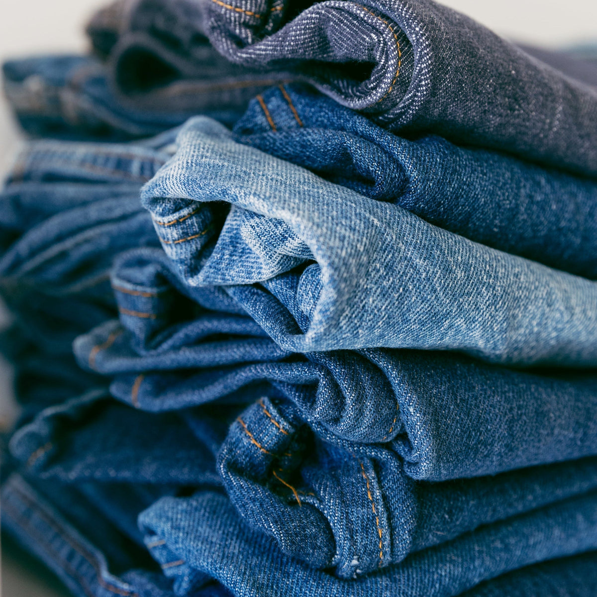 A pile of denim jeans in different shades of blue, showcasing various denim styles and washes