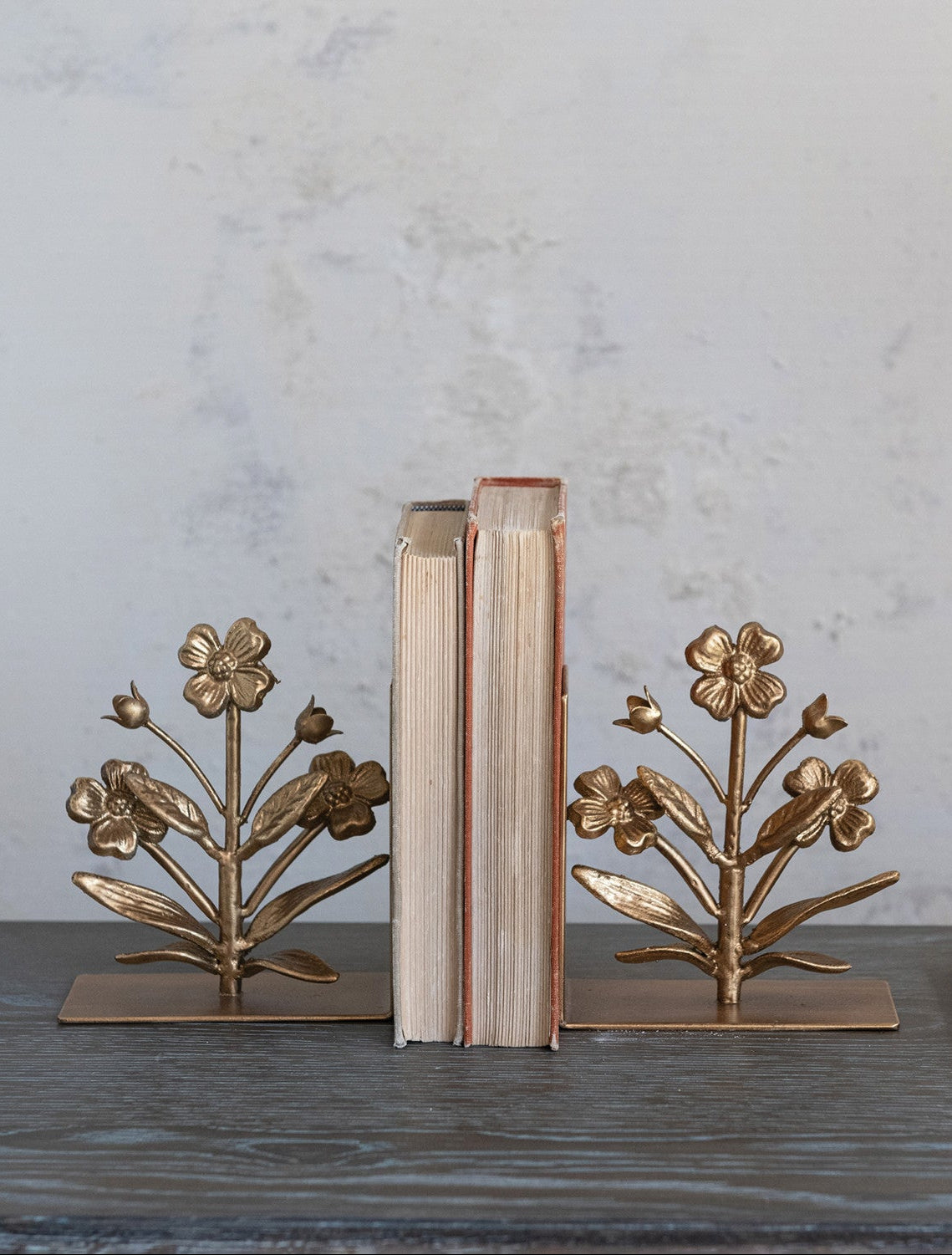 Bronze floral bookends holding books on a wooden surface with a gray marble background