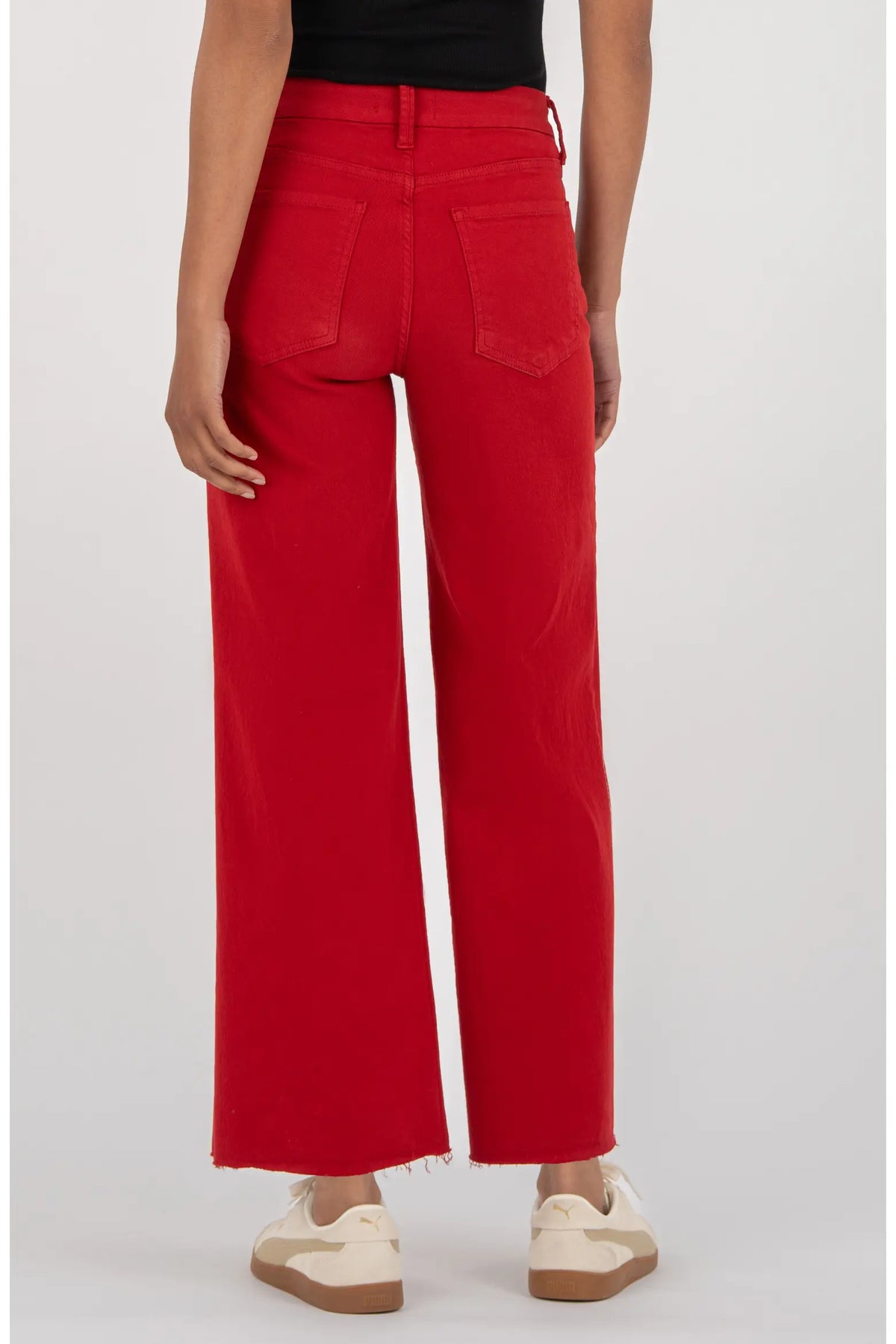 A model shown from the back wearing bright red wide-leg cropped jeans, a black top, and cream sneakers against a light gray studio background.
