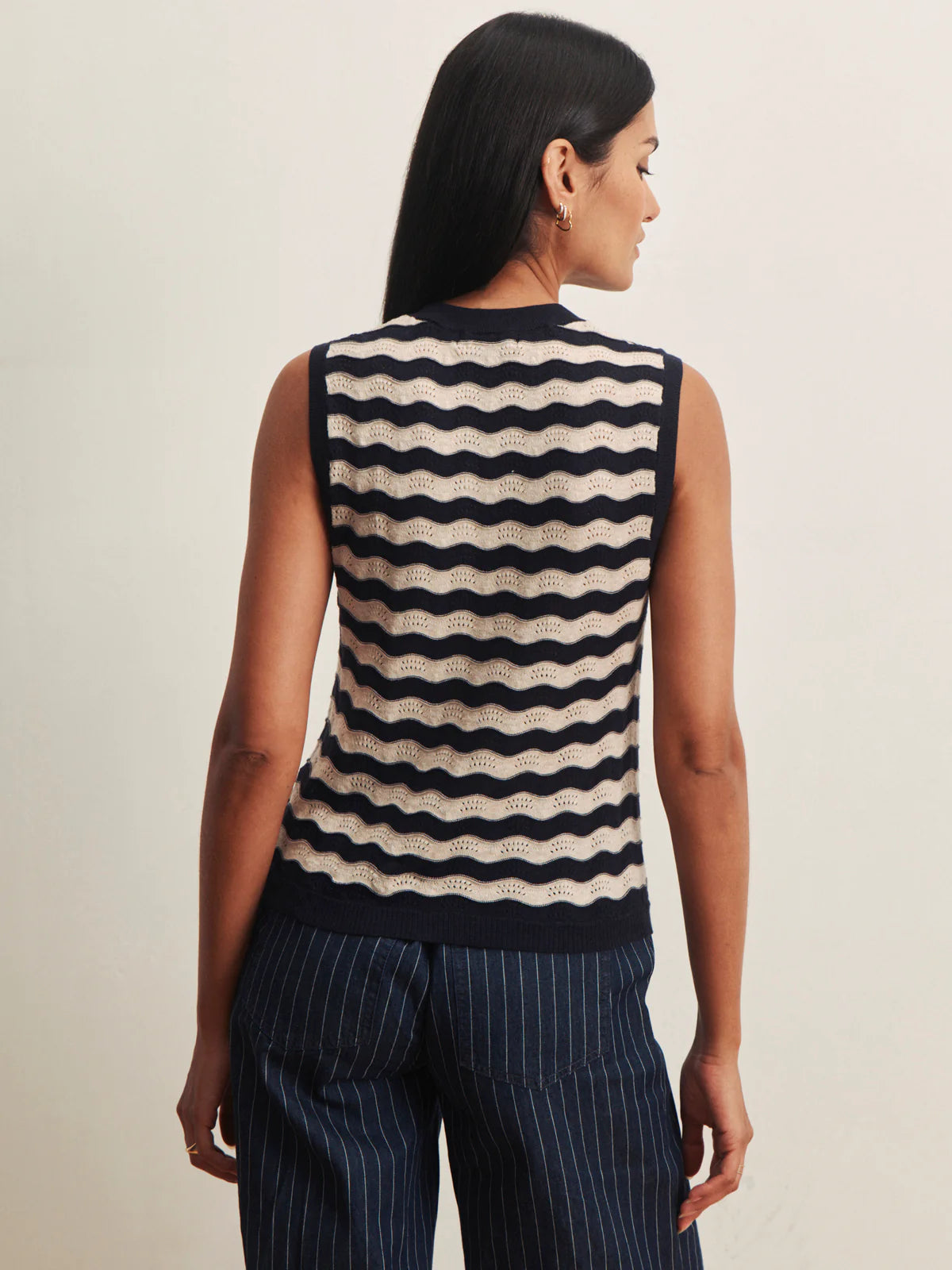 Woman wearing a sleeveless striped top and pinstripe pants against a neutral background