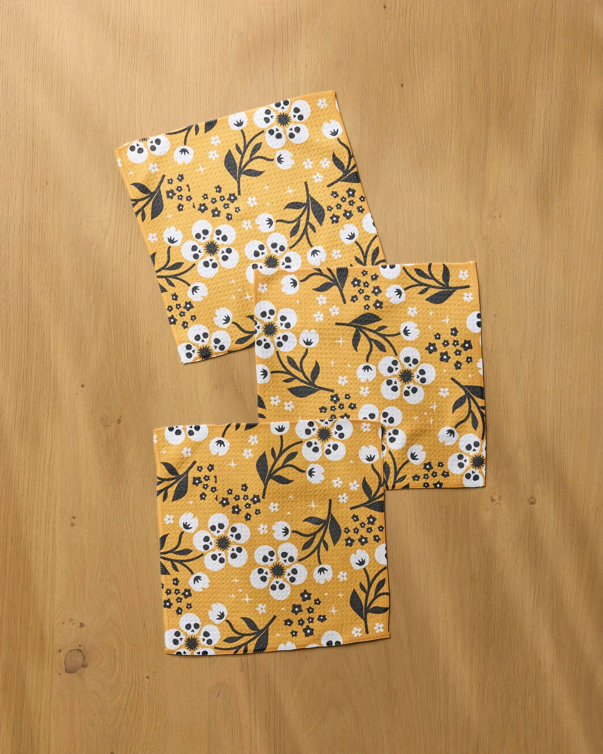 Three square fabric napkins with a yellow floral pattern, laid out on a light wood surface.