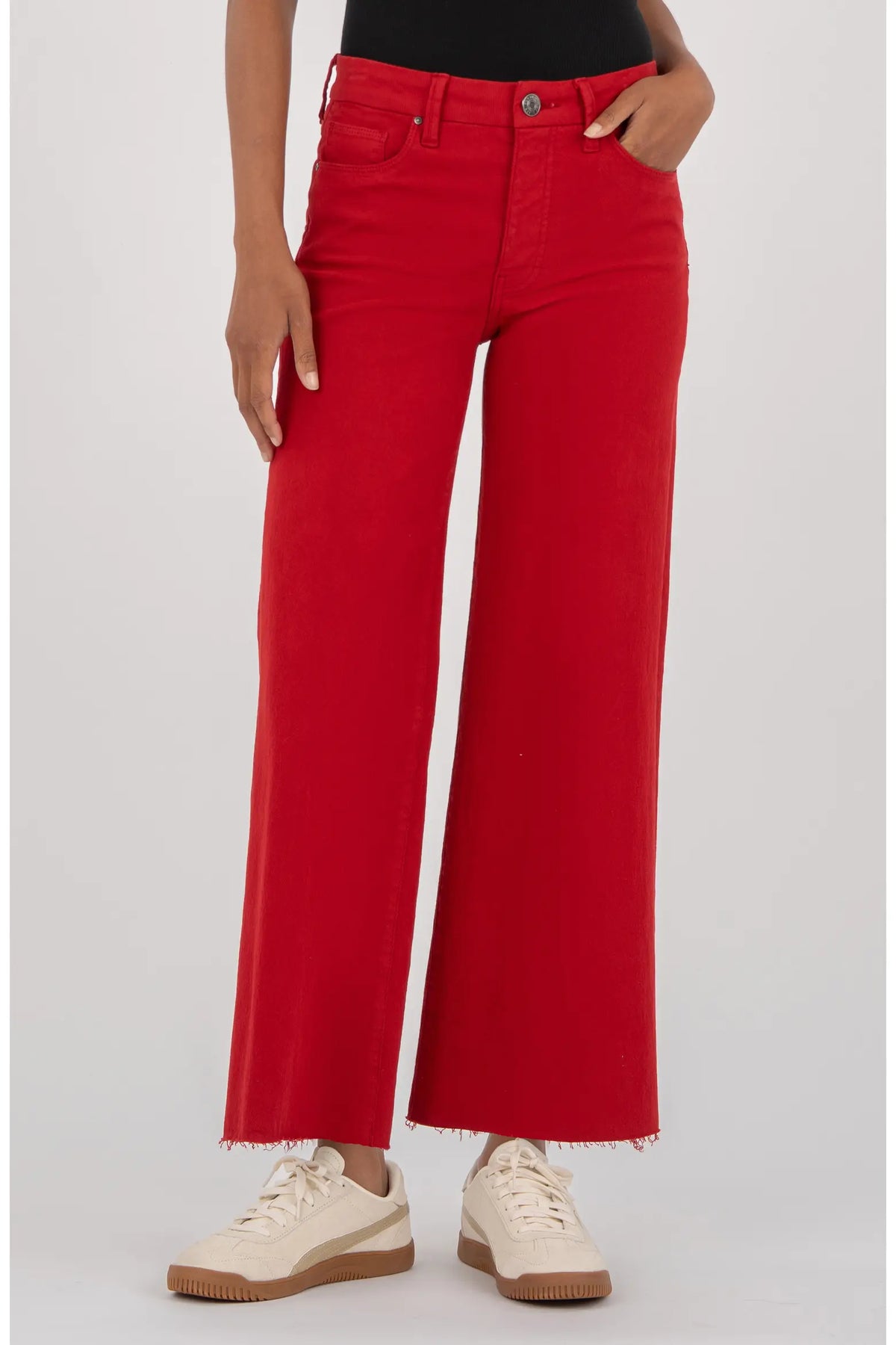 A model wearing bright red wide-leg cropped jeans with a frayed hem, paired with cream sneakers, shown from the waist down against a light gray studio background.