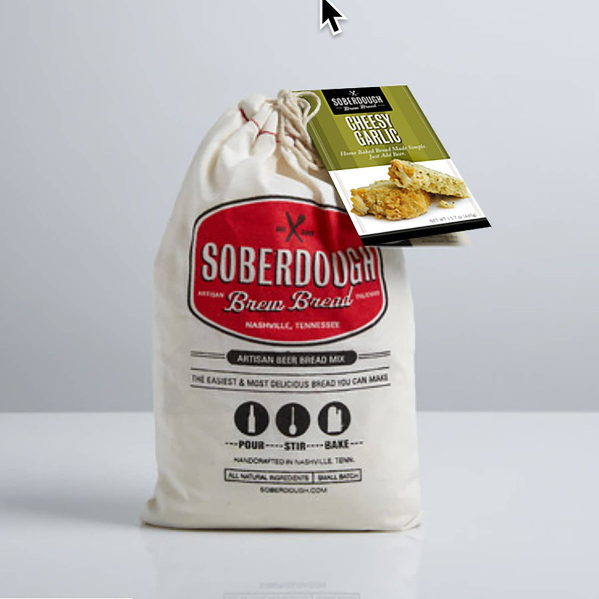A drawstring bread mix bag labeled Soberdough Brioisse with a hanging product tag reading 'Cheese Garlic Bread,' photographed on a clean light gray studio background.