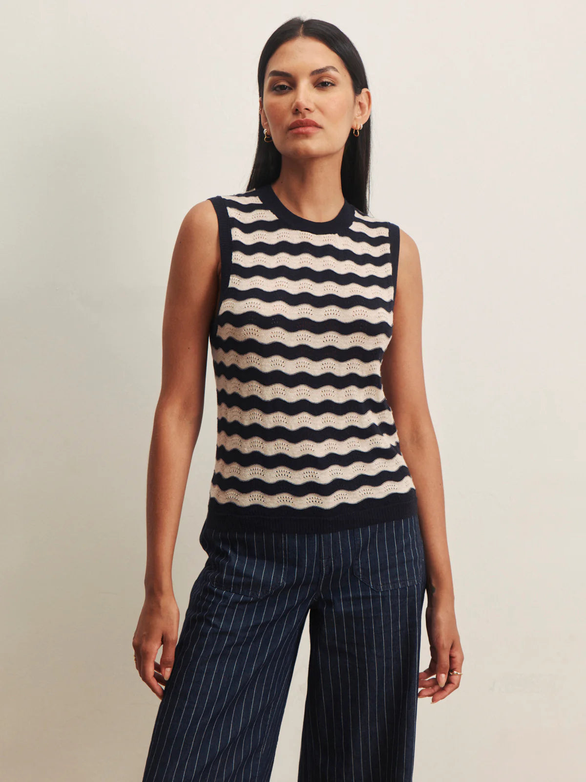 Woman wearing a sleeveless striped top and pinstripe pants on a plain background