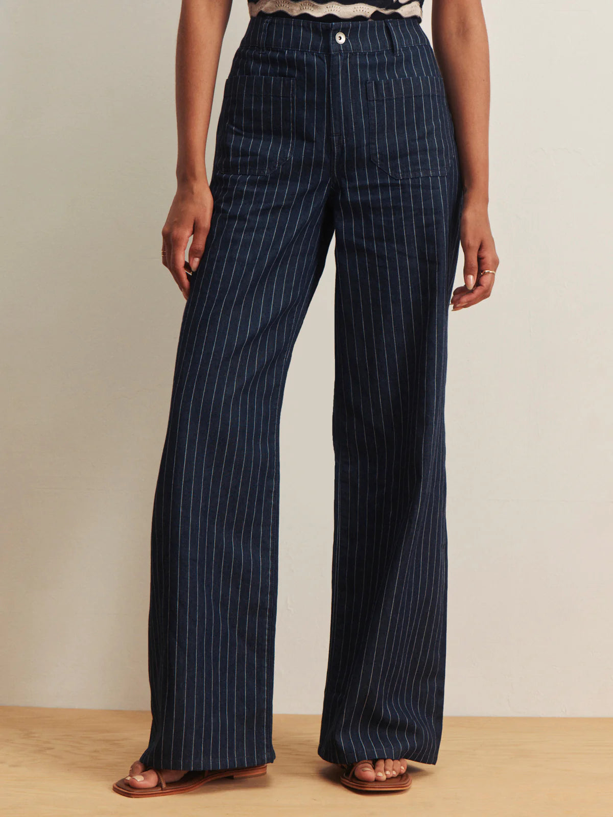 Navy pinstripe pants worn by a person on a beige background