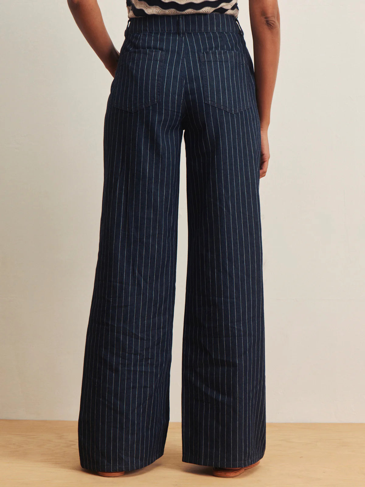 Navy pinstripe pants worn by a person on a beige background